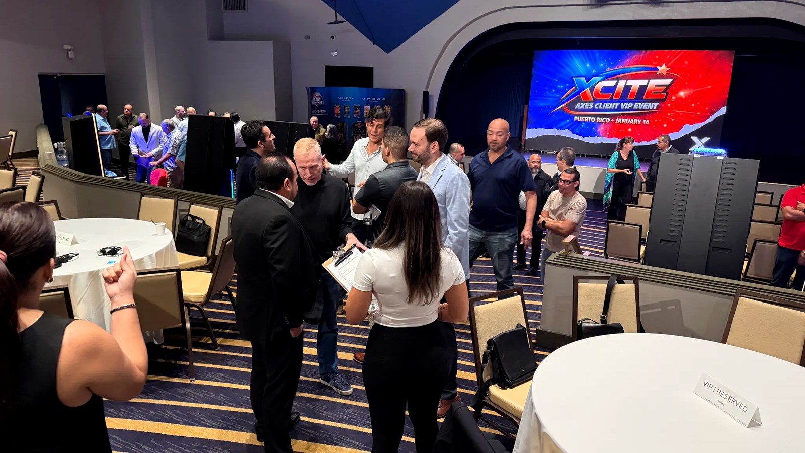 The full room in motion — operators, partners, and AXES executives networking with the XCITE screen lit up behind them.